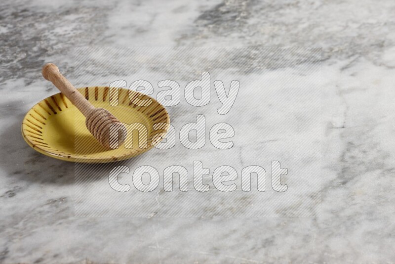 Multicolored pottery plate with wooden honey dipper in it on grey marble background