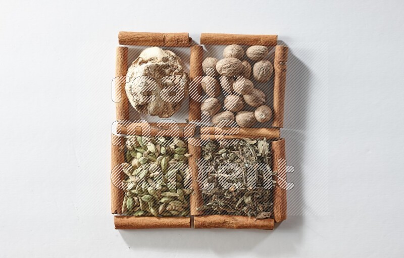 4 مربعات من أعواد القرفة ممتلئة بجوزة الطيب والزنجبيل المجفف والهيل والريحان المجفف على أرضية بيضاء