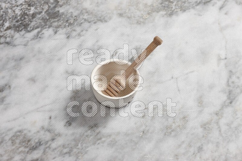 White pottery bowl with wooden honey dipper in it on grey marble background