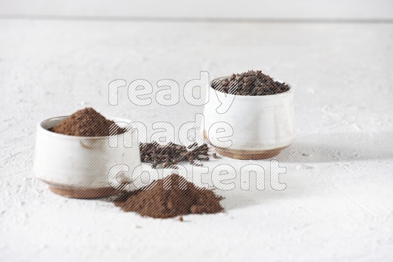 2 Beige ceramic bowls, one full of cloves and the other full of powder on textured white flooring