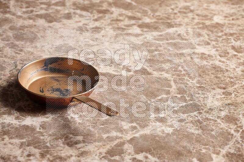 A small copper pan on beige marble background