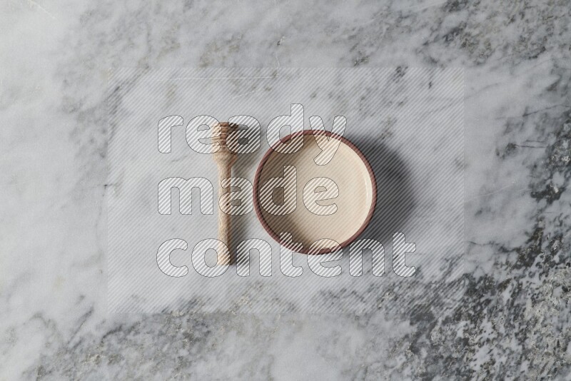 Beige pottery oven bowl with wooden honey dipper on the side on grey marble background