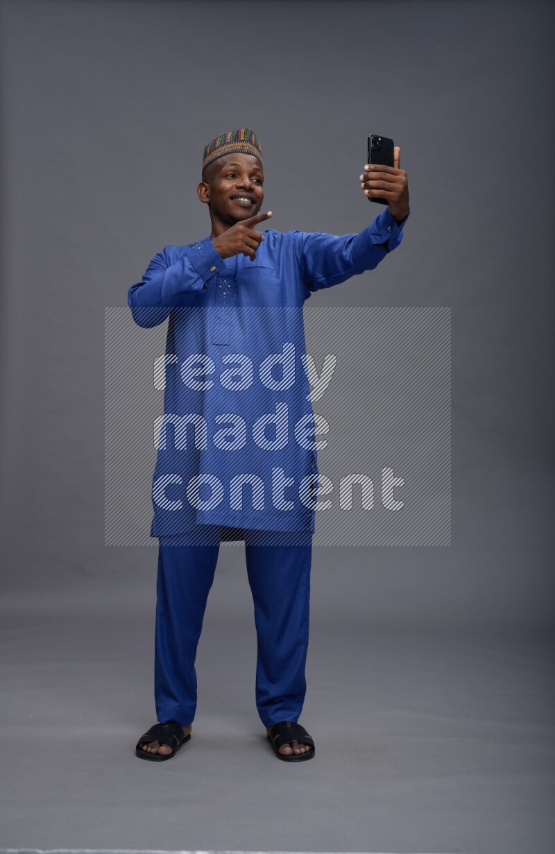 Man wearing Nigerian outfit standing taking selfie on gray background