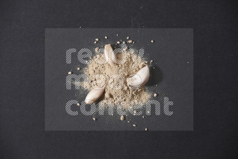 A small pile of garlic powder with some of cloves and a whole garlic bulb on a black flooring