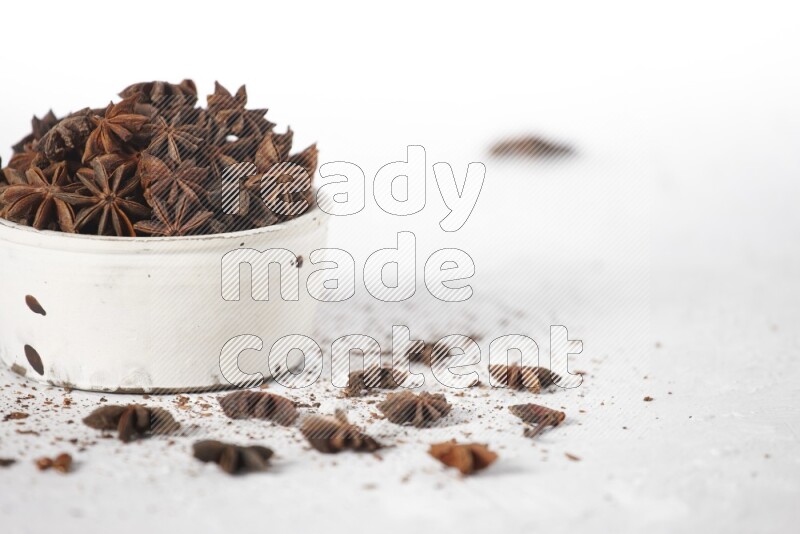 Star Anise in a white bowl and more of it sprinkled on white background
