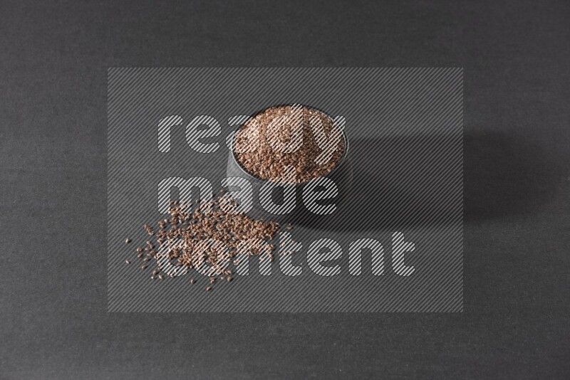 وعاء فخاري أسود ممتلئ بحبوب بذر الكتان محاط بالبذور على أرضية سوداء