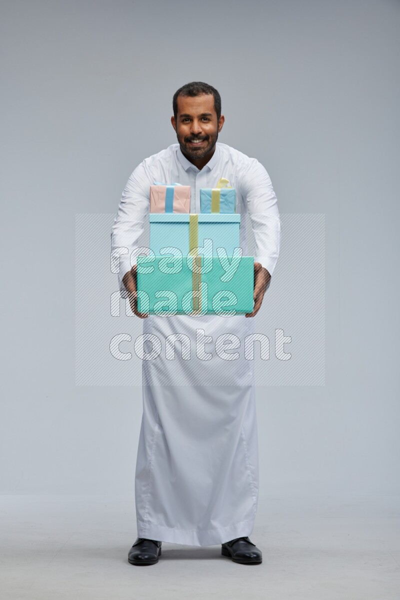 Saudi man Wearing thob standing holding gift box on Gray background