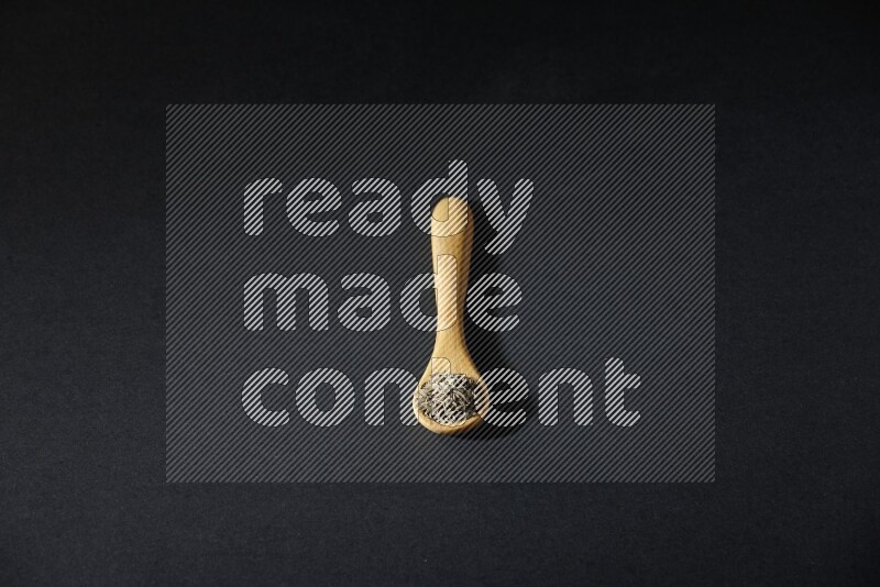 ملعقة خشبية ممتلئة بحبوب الكمون على خلفية سوداء