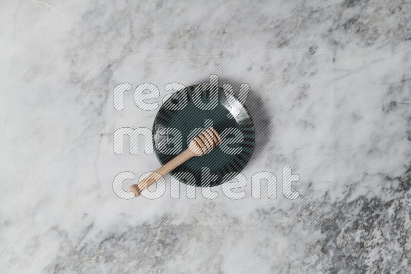 Multicolored pottery plate with wooden honey dipper in it on grey marble background