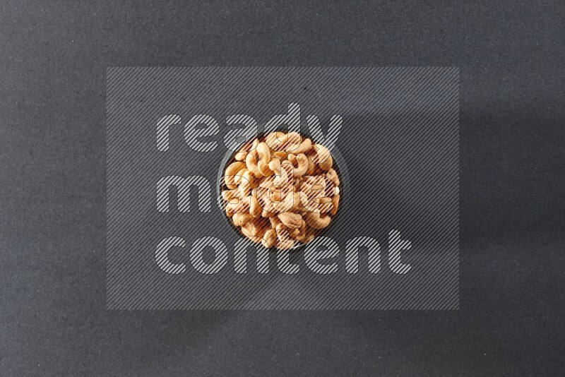 A black pottery bowl full of cashews on a black background in different angles