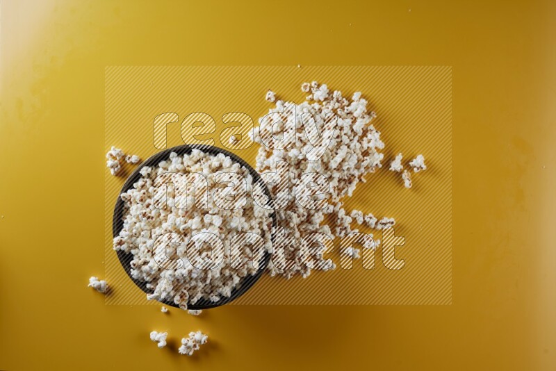 A copper ceramic bowl full of popcorn with popcorn beside it on a yellow background in different angles