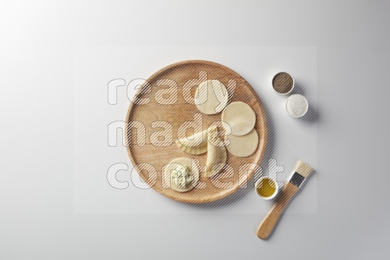 two closed sambosas and one open sambosa filled with cheese while salt, black pepper and oil with oil brush aside in a wooden dish on a white background