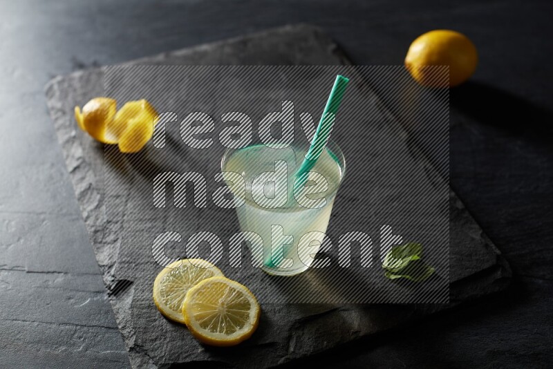 A glass of lemon juice with a straw on black background
