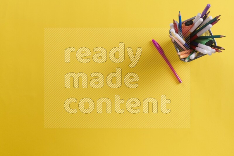 Pens, pencils and school supplies in a metal pen holder on yellow background