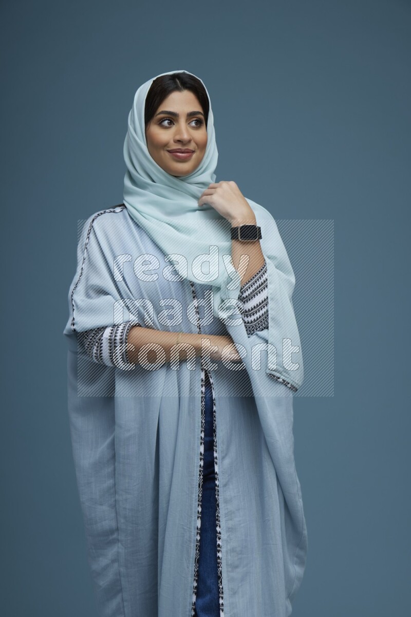 A woman posing in a blue background wearing a blue Abaya with hijab