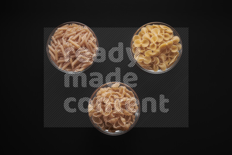 Different pasta types in glass bowls on black background
