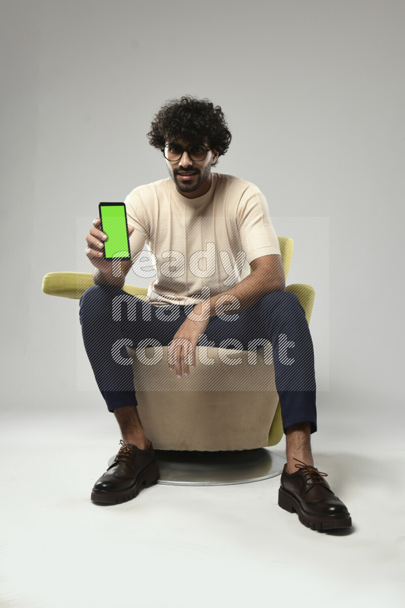 A man wearing casual sitting on a chair showing a phone screen on white background