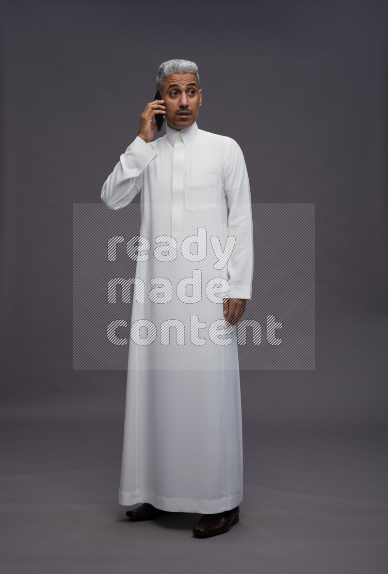 Saudi man wearing thob standing talking on phone on gray background