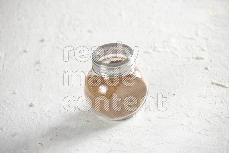 Herbs glass jar full of cinnamon powder on a textured white background