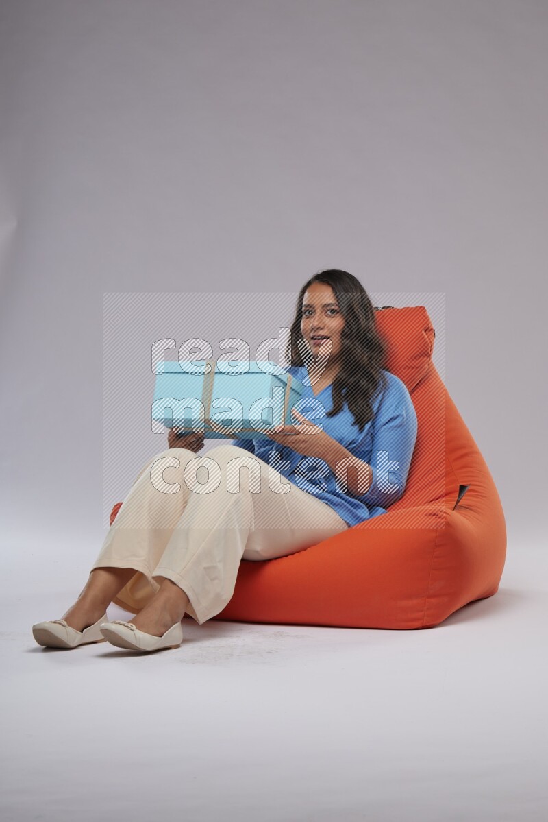 A woman sitting on an orange beanbag and opining a gift