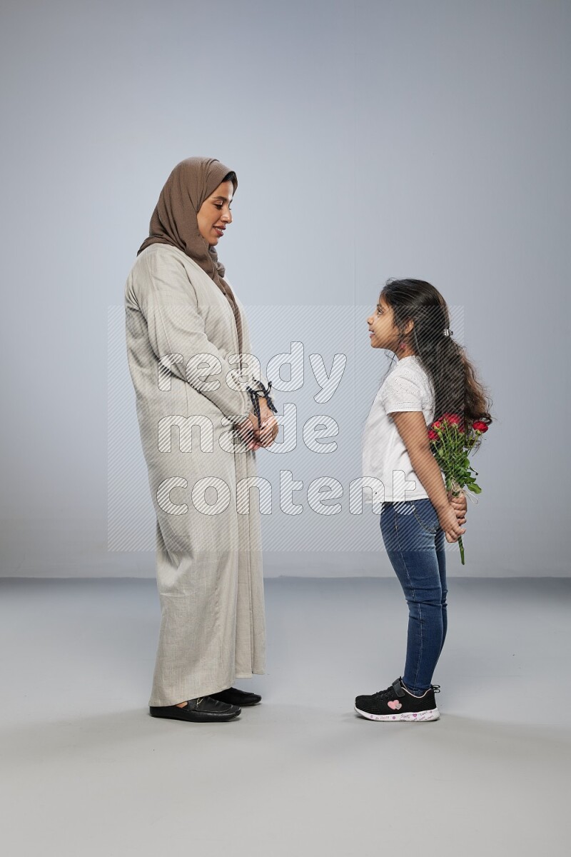 A girl standing giving flowers to her mother on gray background