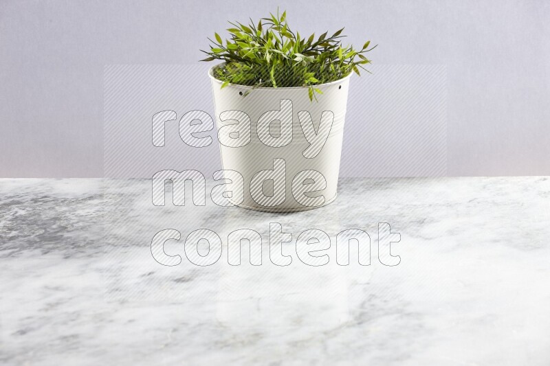 Green artificial plant in white pot on light grey marble background