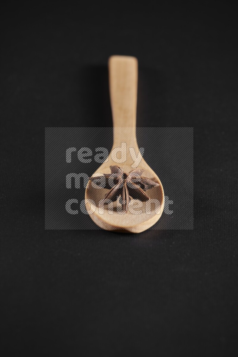 اليانسون النجمي في ملعقة خشبية فوق اليانسون النجمي الذي يغطي الإطار على أرضية سوداء