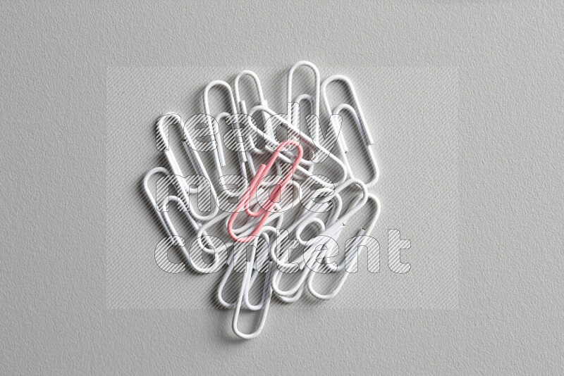 A bunch of white paper clips with a different colored paper clip in the center on grey background