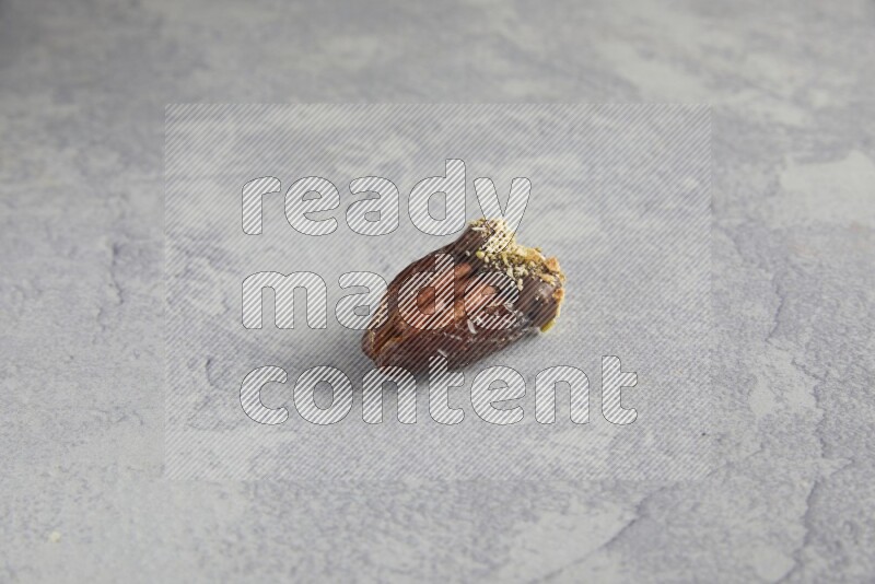 pecan stuffed date covered with Dark chocolate and chopped pistachios on alight grey background