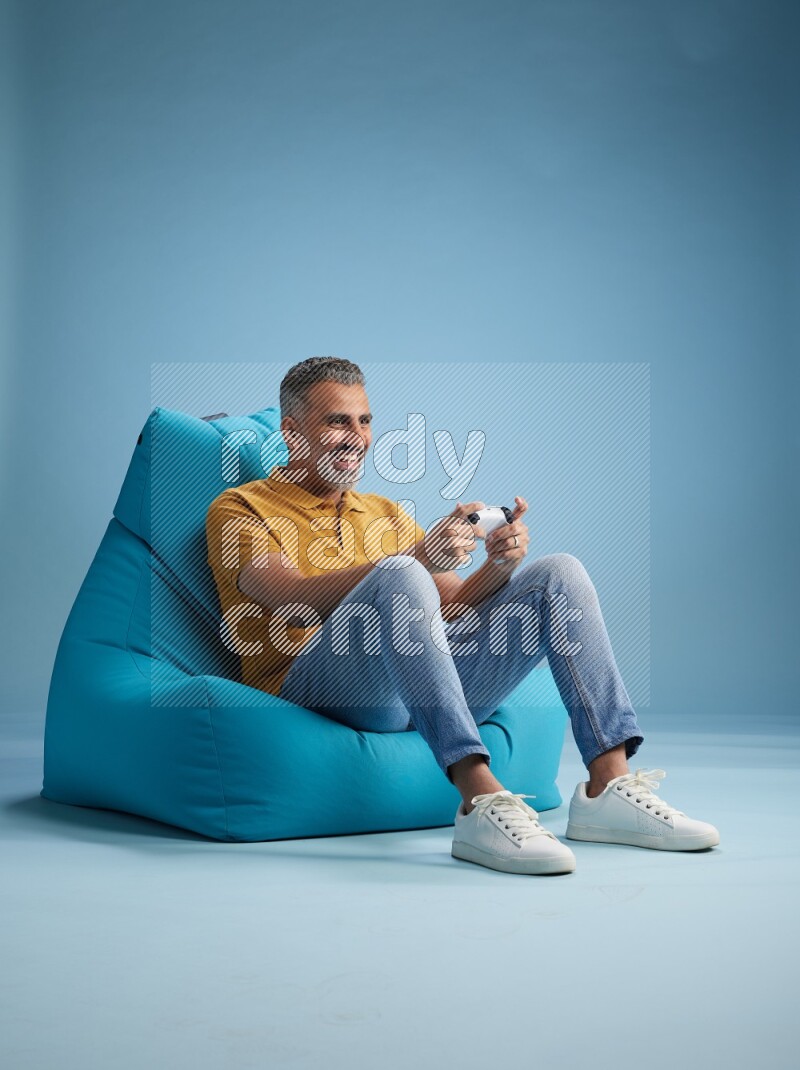 A man sitting on a blue beanbag and gaming with joystick