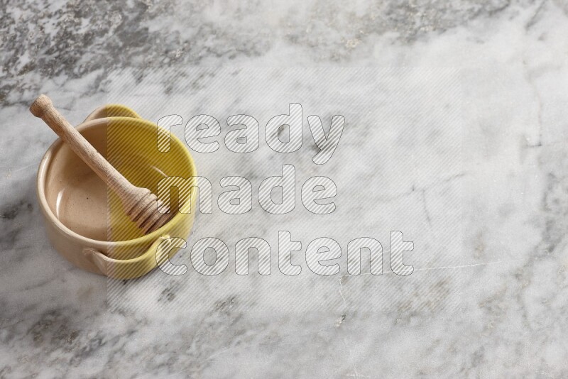 Multicolored pottery bowl with wooden honey dipper in it on grey marble background