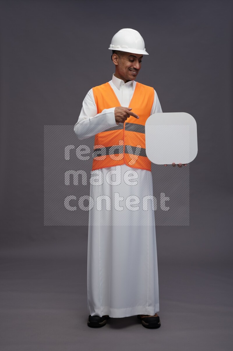 Saudi man wearing thob with engineer vest standing holding social media sign on gray background