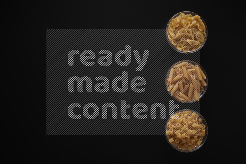 Different pasta types in 3 glass bowls on black background