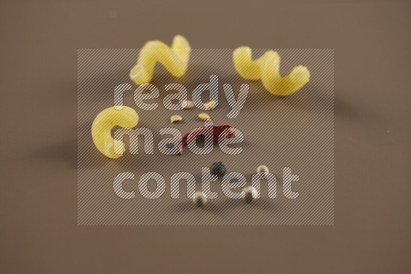 Raw pasta with different ingredients such as cherry tomatoes, garlic, onions, red chilis, black pepper, white pepper, bay laurel leaves, rosemary and cardamom on beige background