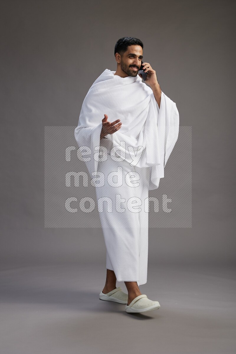 A man wearing Ehram Standing talking on phone on gray background