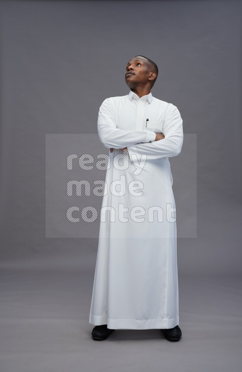 Saudi man wearing thob standing with crossed arms on gray background