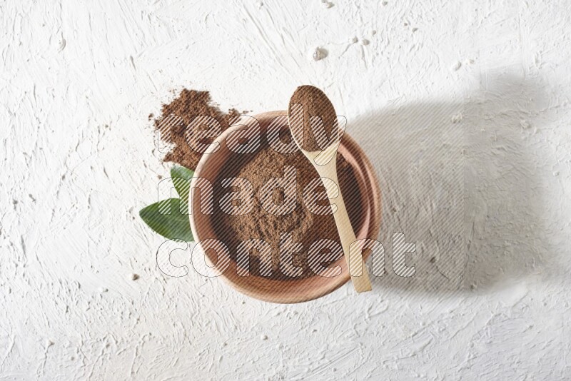A wooden bowl and a wooden spoon full of cloves powder on a textured white flooring
