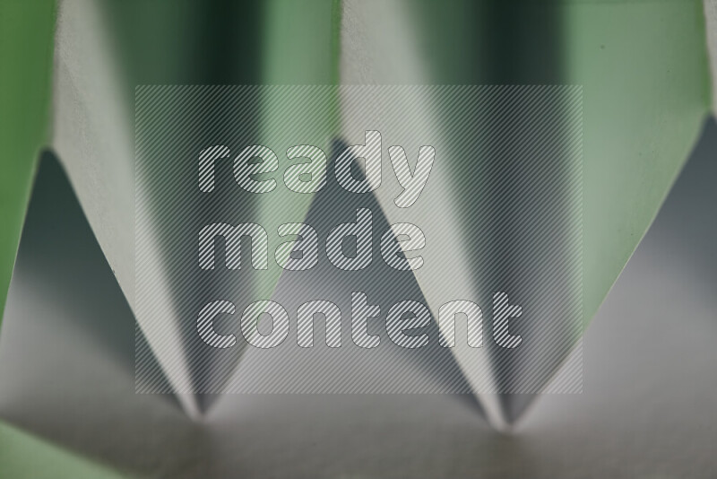 A close-up abstract image showing sharp geometric paper folds in white and green gradients
