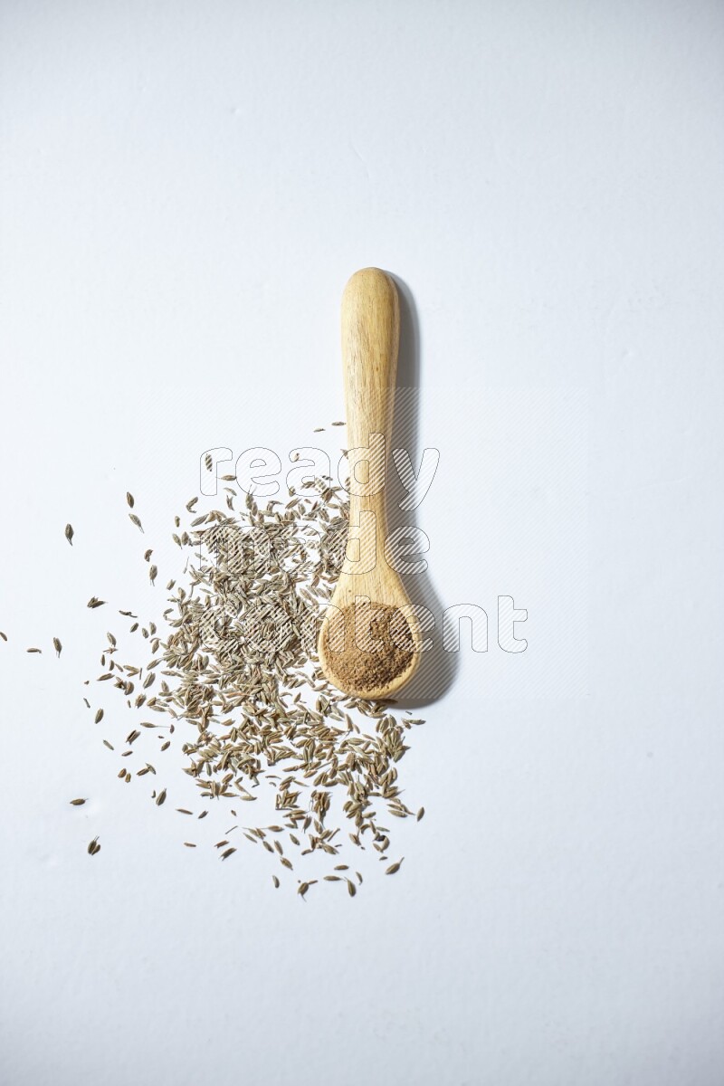 A wooden spoon full of cumin powder and cumin seeds beside it on white flooring