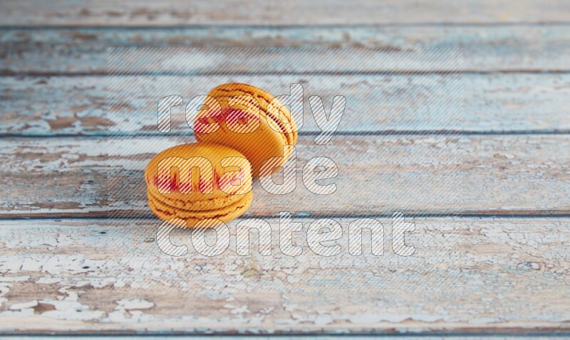 45º Shot of two orange Exotic macarons on light blue wooden background