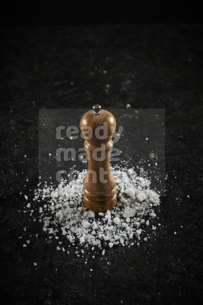 A wooden grinder standing upright and surrounded by coarse white sea salt on black background