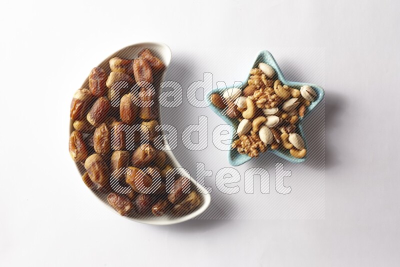Dates in a crescent pottery plate and a star shaped plate with mixed nuts on white background