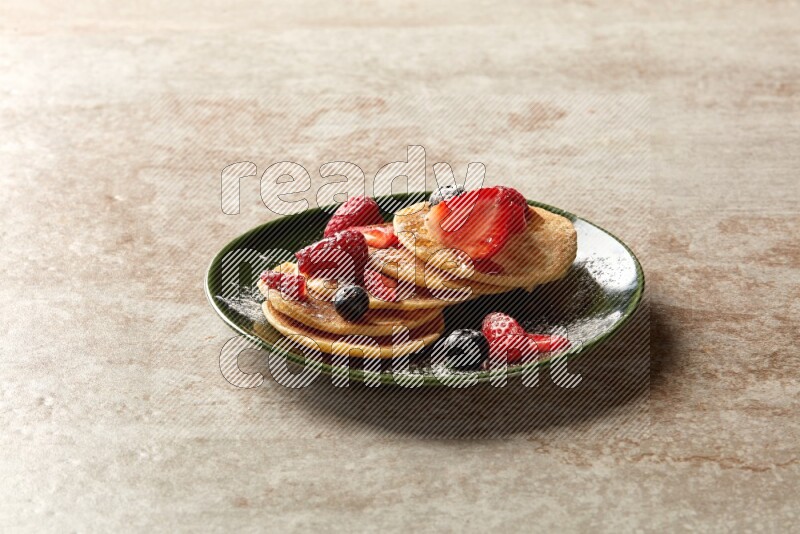Five stacked mixed berries mini pancakes in a green plate on beige background