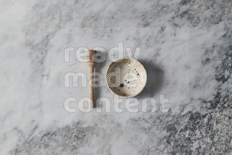 Multicolored pottery bowl with wooden honey dipper on the side on grey marble background