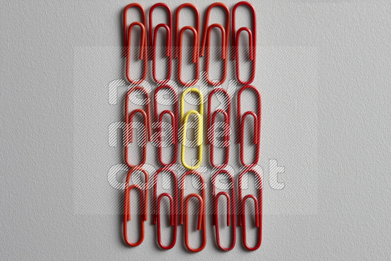 A bunch of red paper clips with a different colored paper clip in the center on grey background