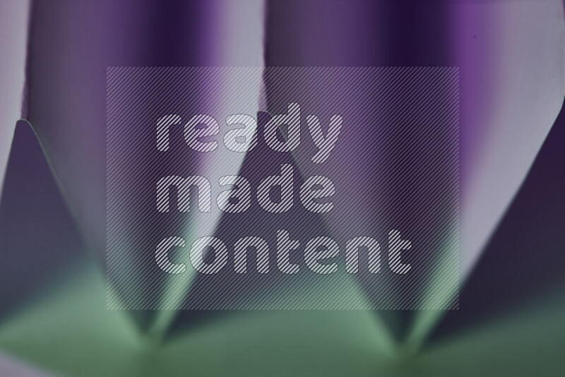 A close-up abstract image showing sharp geometric paper folds in green and purple gradients
