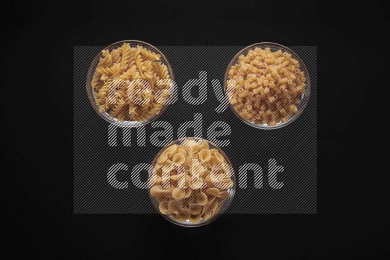 Different pasta types in glass bowls on black background