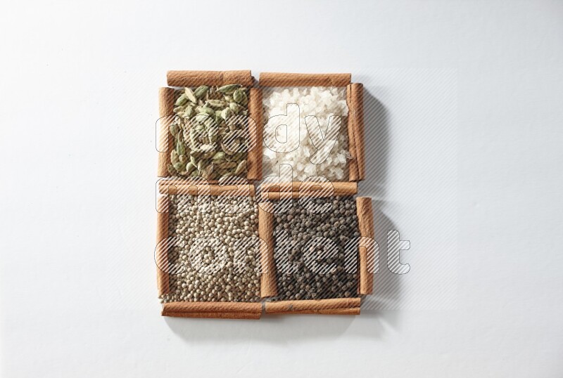 4 مربعات من أعواد القرفة ممتلئة بالهيل والملح والفلفل الأبيض والفلفل الأسود على أرضية بيضاء