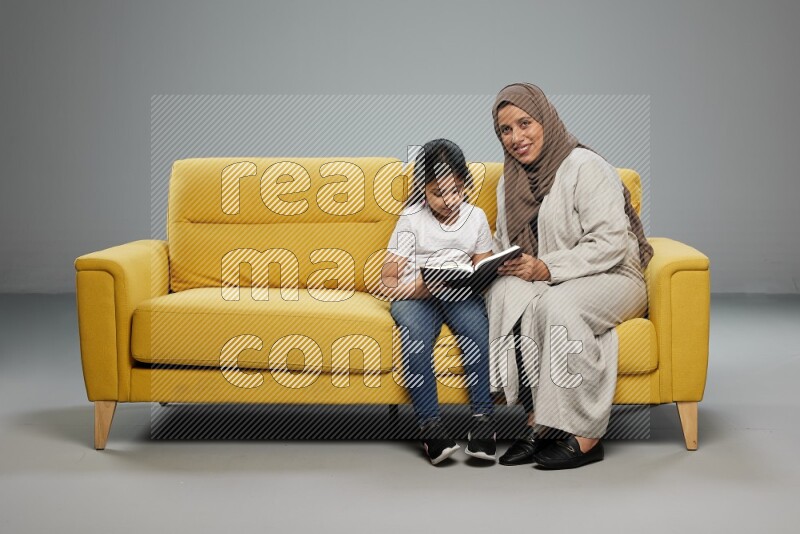 Mom and daughter sitting reading a book on gray background