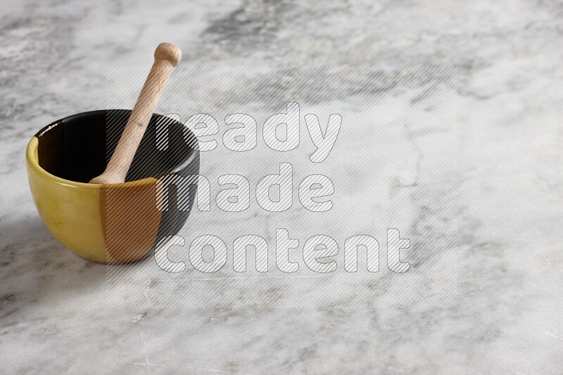 Multicolored pottery bowl with wooden honey dipper in it on grey marble background
